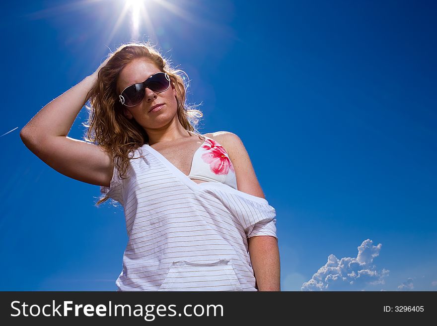 Attractive redhaired woman with freckles. Looking cool with big sunglasses, casual wear and bikini into camera. Deep blue sky with Lensflares. Attractive redhaired woman with freckles. Looking cool with big sunglasses, casual wear and bikini into camera. Deep blue sky with Lensflares