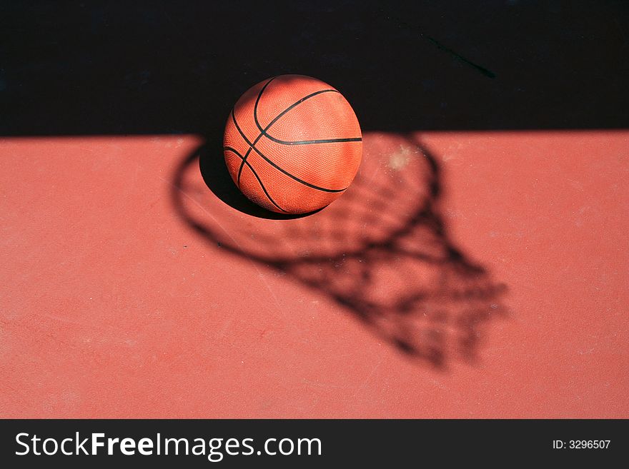 A Basketball and net shadow on a red court