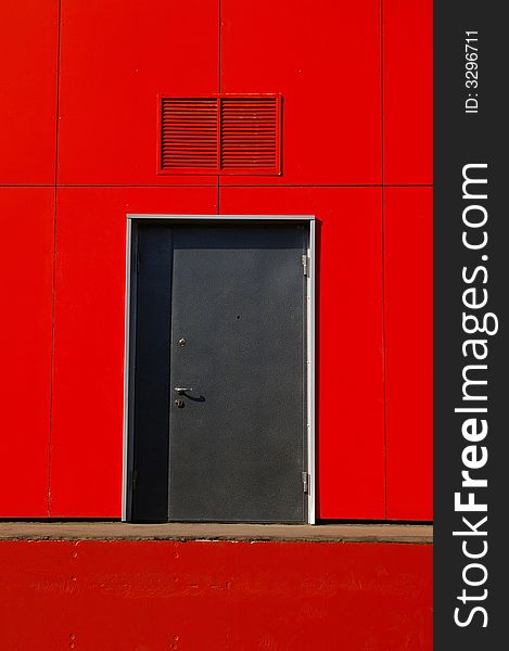 Grey door in a red wall, a part of a building