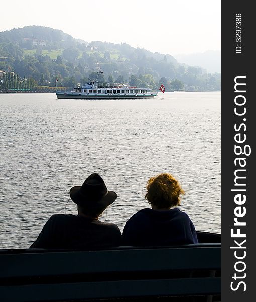 Couple sitting on a bench in switzerland watching a ship passing by. Couple sitting on a bench in switzerland watching a ship passing by