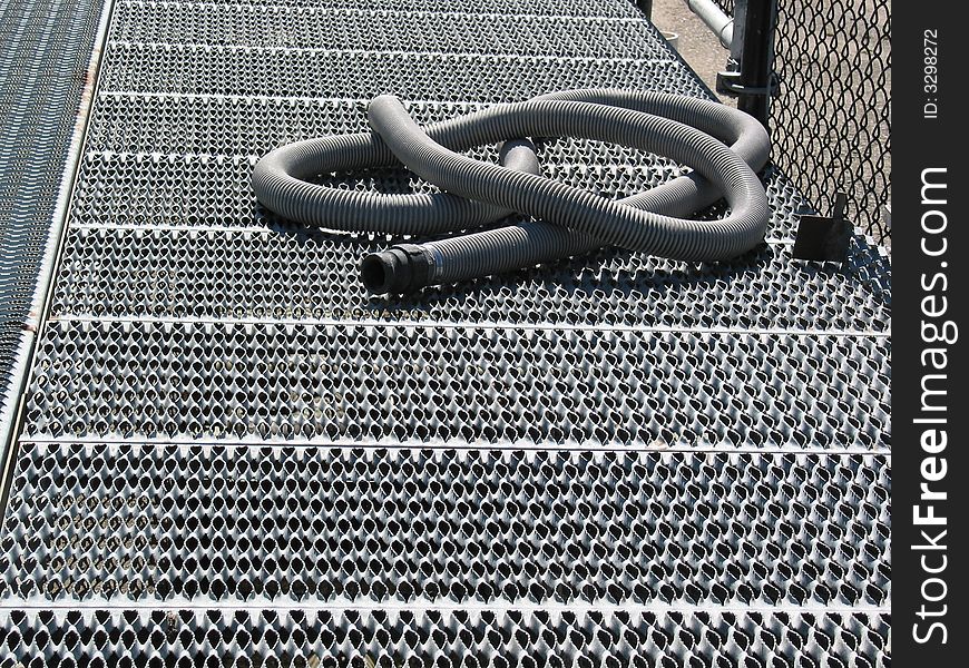 A gray hose is coiled on metal grating at a fish hatchery. A gray hose is coiled on metal grating at a fish hatchery.