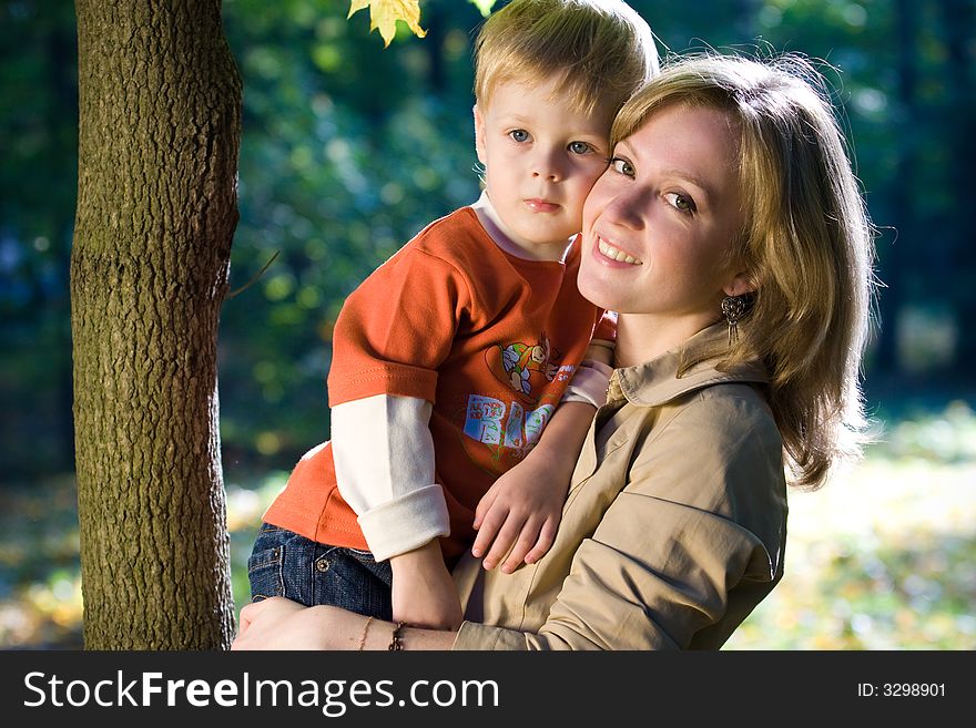 Laughing mother holds son in autumn park