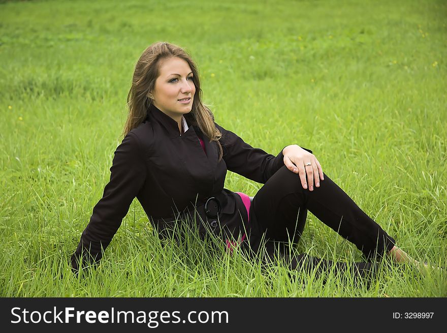 The beautiful girl sits on a green grass. The beautiful girl sits on a green grass