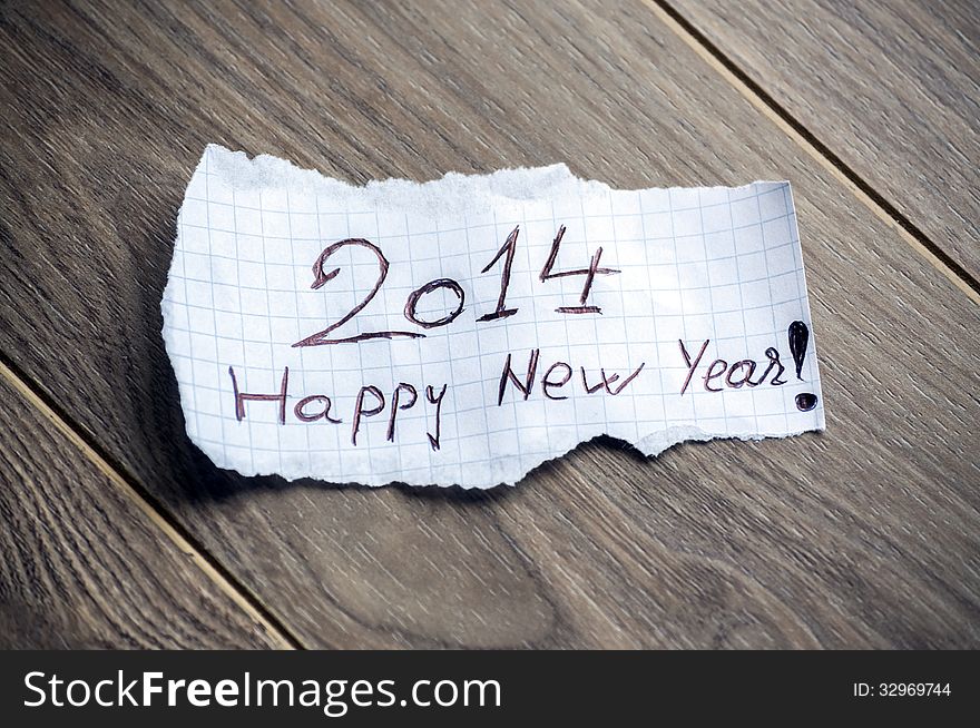 Happy new Year 2014 - Hand writing text on a piece of paper on wood background