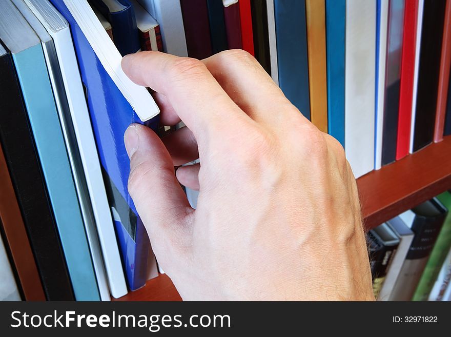 A close-up of man's hand, which select a book from the bookshelf. A close-up of man's hand, which select a book from the bookshelf.