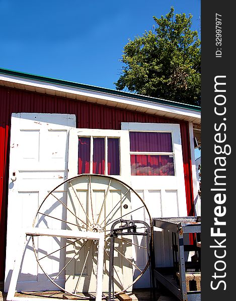 Bright white antique doors and wheel and frame against red garage and blue sky. Bright white antique doors and wheel and frame against red garage and blue sky.