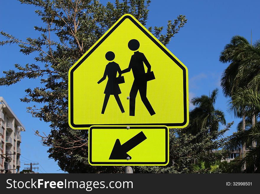 Pedestrian crossing sign in front of blue sky and trees