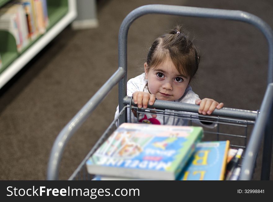 Preschool girl carry books in a cart at the library. Preschool girl carry books in a cart at the library.