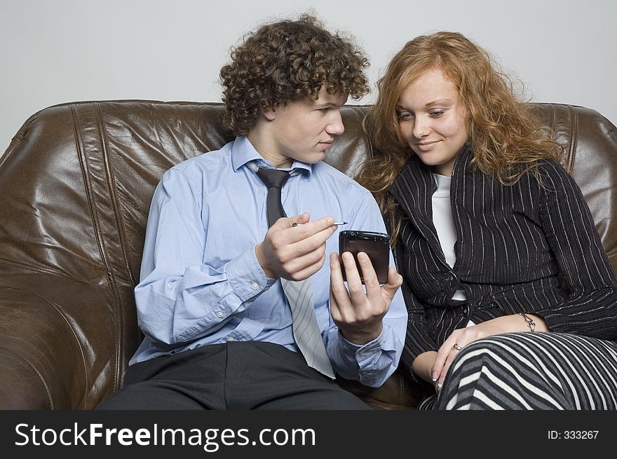 (Boy in relaxed office attire) Boy sitting on a leather couch is showing a girl beside him something on his palmtop. (Boy in relaxed office attire) Boy sitting on a leather couch is showing a girl beside him something on his palmtop