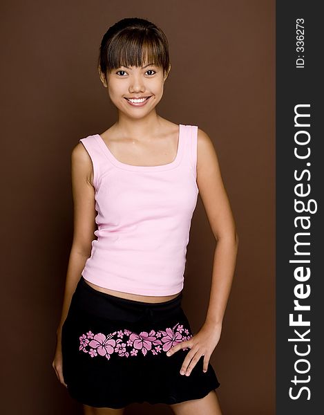 A cute young asian woman in a pink top on brown background. A cute young asian woman in a pink top on brown background