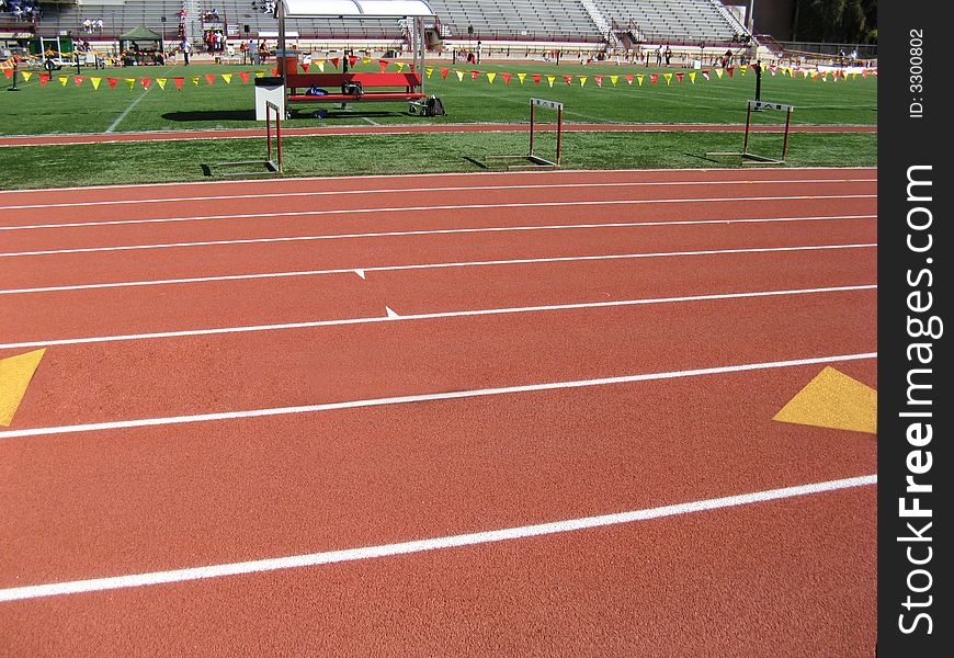 Close up of track lanes.  Grass field and bleachers in background.