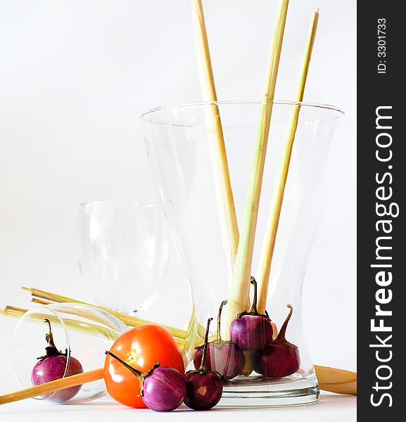 Still life of the ingredients of green curry, namely lemon grass, mini brinjals, or eggplant, and a single tomato, in various glassware including wine glasses. Still life of the ingredients of green curry, namely lemon grass, mini brinjals, or eggplant, and a single tomato, in various glassware including wine glasses.