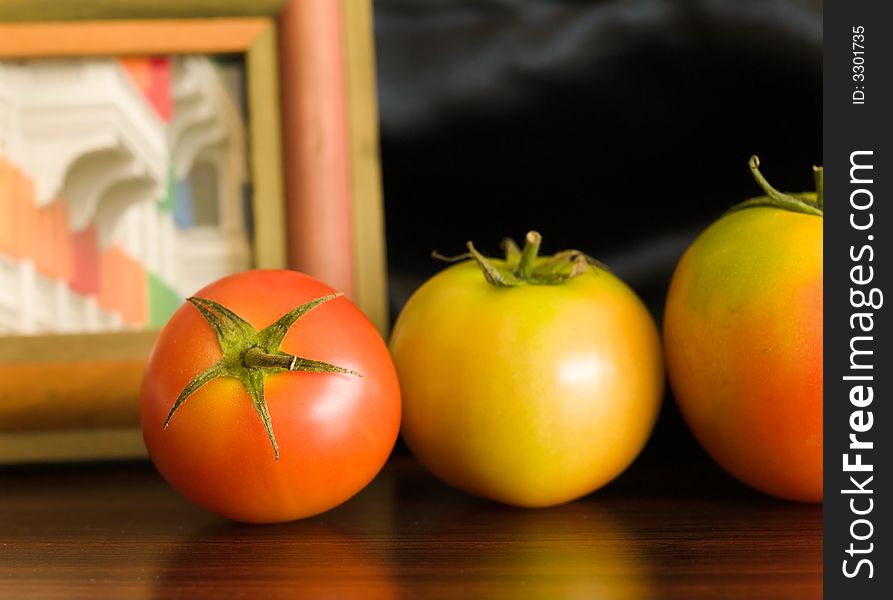 Still life of a row of tomatoes of increasing sizes against a framed picture on a black back drop. Still life of a row of tomatoes of increasing sizes against a framed picture on a black back drop