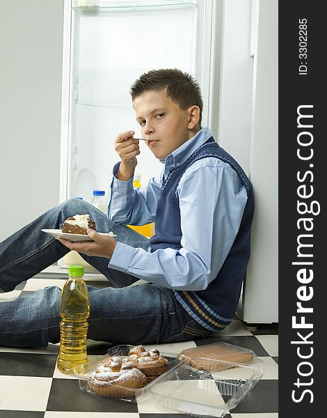 Boy sitting on the floor and eating cake. Side view. Looking at camera. Boy sitting on the floor and eating cake. Side view. Looking at camera.