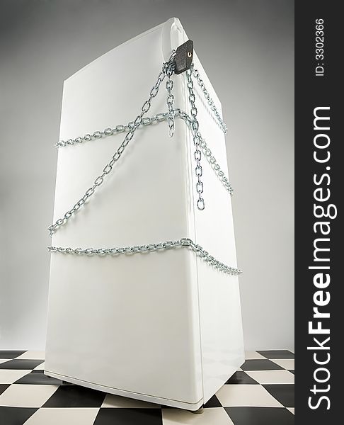 Closed fridge enwinded by chain and lock. Grey background. Low angle view. Closed fridge enwinded by chain and lock. Grey background. Low angle view