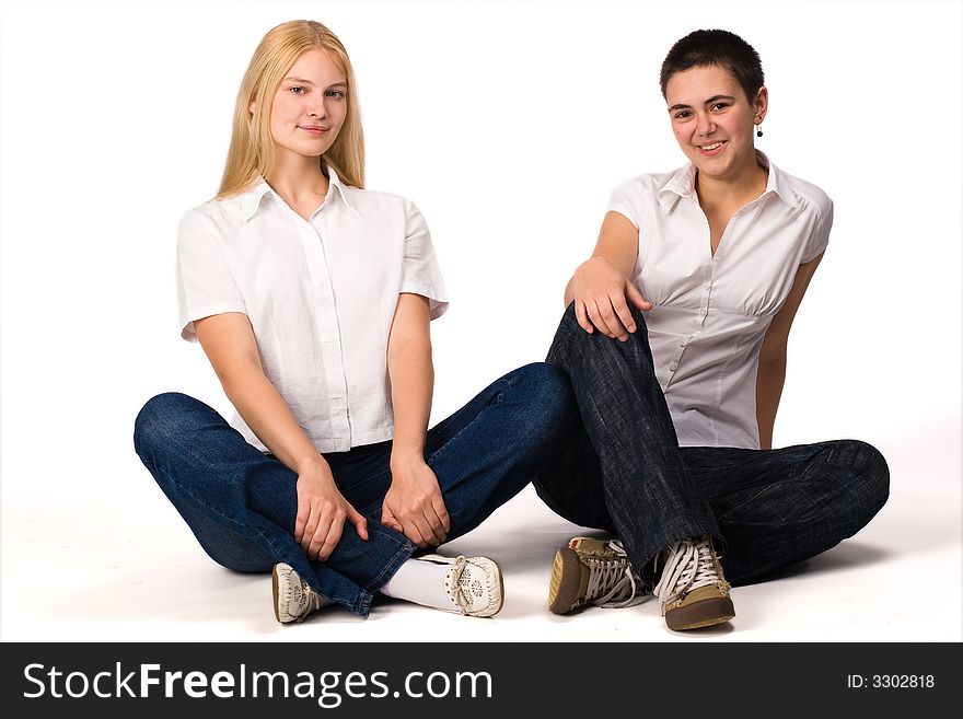 Two young girls blonde and brunette sits on the floor on white background