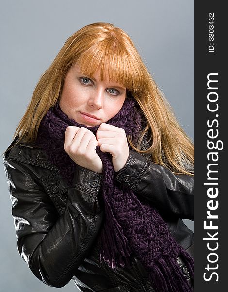 Attractive woman, huddling into her muffler with black leatherjacket. Gray background. Attractive woman, huddling into her muffler with black leatherjacket. Gray background.