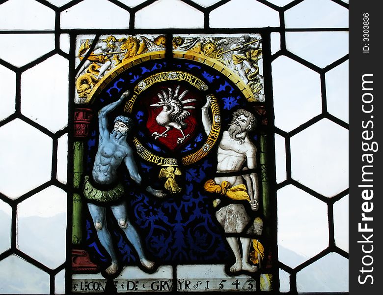 Stained glass found in the castle of Gruyeres. It represents an emblem with two men holding a gold ring with a bird in its center.
