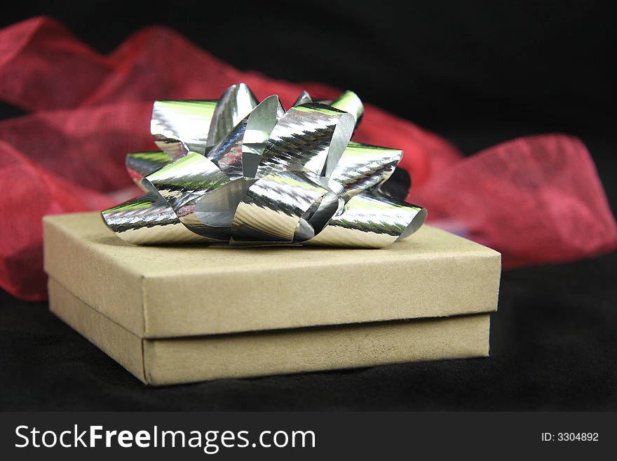 Gift box with silver bow on top with black background and red fabric behind