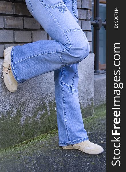 Close-up image of a teenager legs wearing bluejeans near a building wall. Close-up image of a teenager legs wearing bluejeans near a building wall.