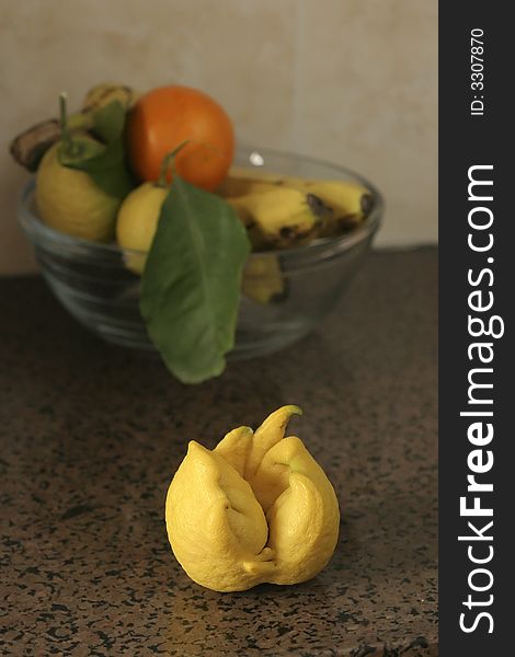 Unusual shaped lemon in front of glass bowl with bananas,clementino and lemons. Unusual shaped lemon in front of glass bowl with bananas,clementino and lemons