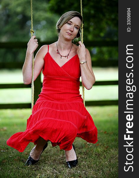 Young woman sat on a swing wearing a red dress. Young woman sat on a swing wearing a red dress