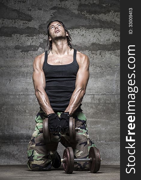 Portrait of handsome athlete lifting weights on wall background