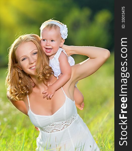 Happy family on nature outdoors mother and baby daughter on the green meadow in a white dress. Happy family on nature outdoors mother and baby daughter on the green meadow in a white dress