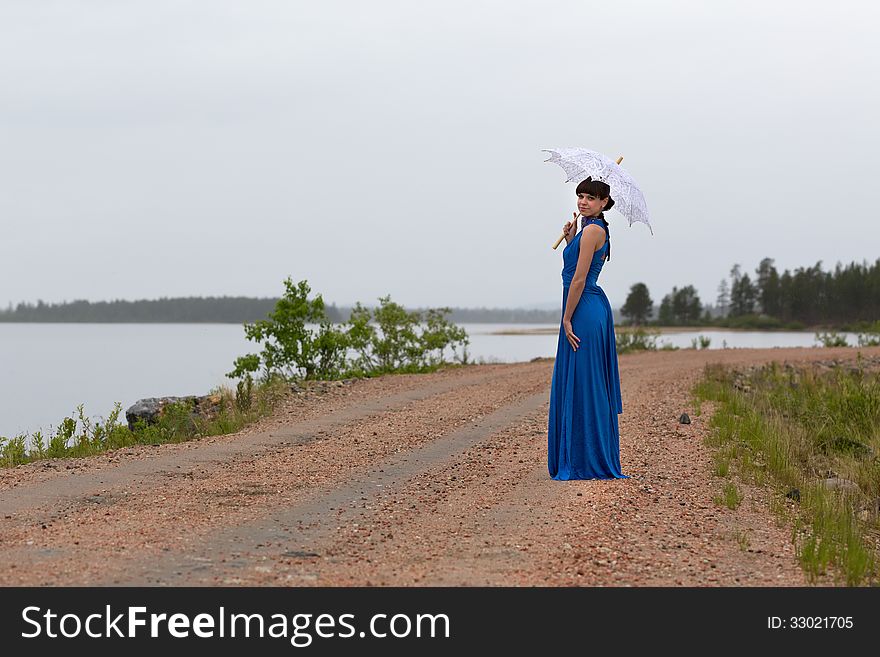 Beautiful girl in a blue dress with an umbrella on a country road