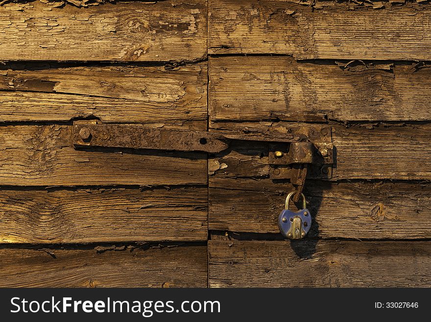 Old rusty padlock on wooden door lit by setting sun. Old rusty padlock on wooden door lit by setting sun