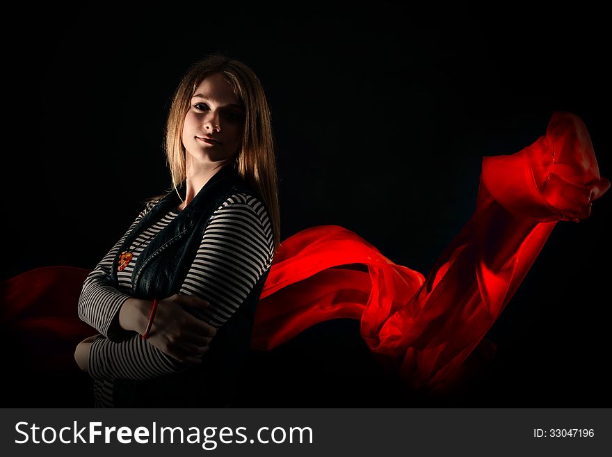 Beautiful girl against red fabric in the dark with long blond hair