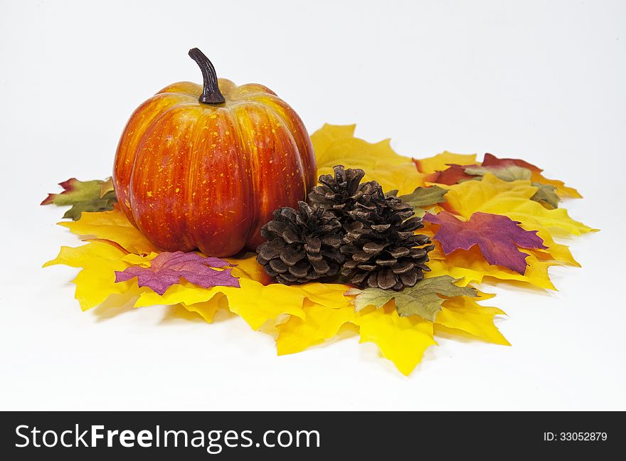 Pumpkin and pine cones on multicolored silk leaves against a white background