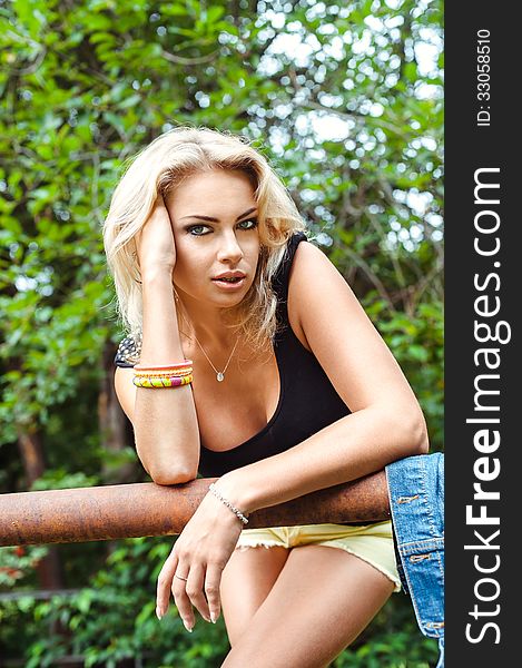 Portrait of blond woman wearing yellow shorts and a black tank-top, outdoors. Portrait of blond woman wearing yellow shorts and a black tank-top, outdoors