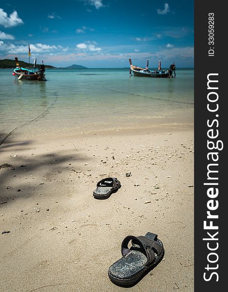 Pair of sandal on the beach with two fishing boat under blue sky