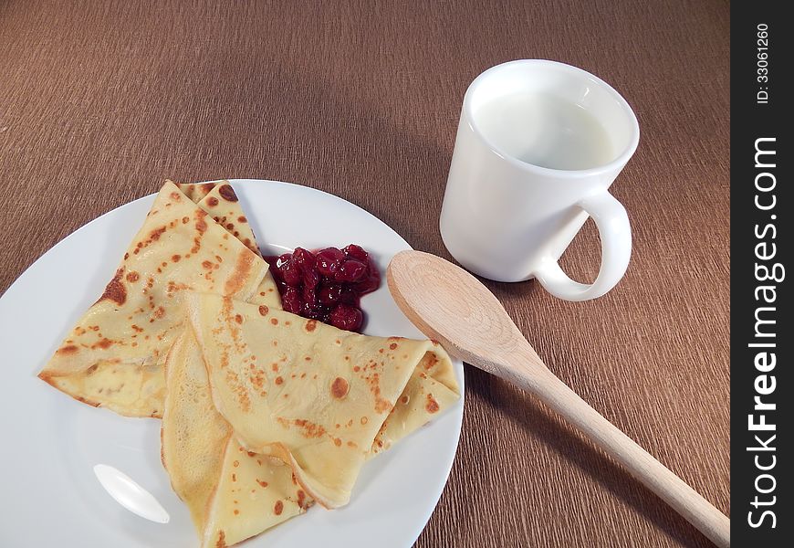 Pancakes with cherry jam on a plate and a cup of milk, breakfast