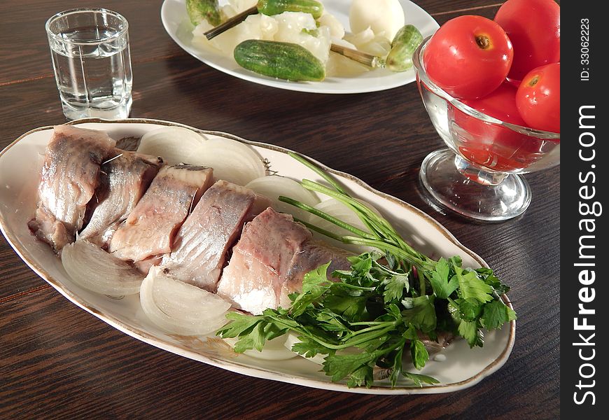 Pickled herring with tomatoes and pickled cabbage, a shot of vodka, wooden table