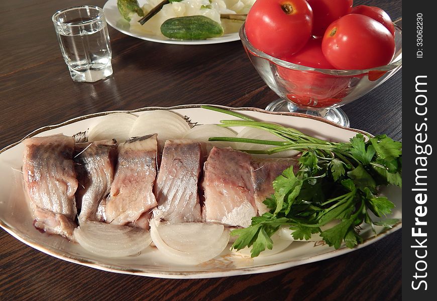 Pickled herring with tomatoes and pickled cabbage, a shot of vodka, wooden table