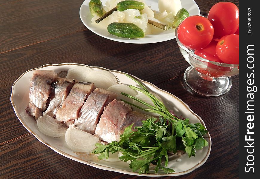Pickled herring with tomatoes and pickled cabbage, wooden table