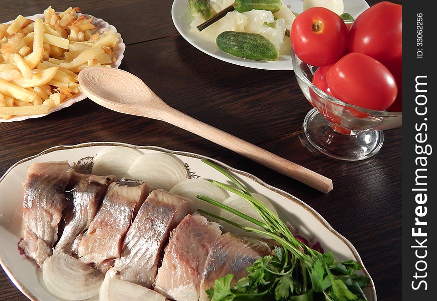 Herring with marinated tomatoes and cabbage, roast potatoes on wooden table