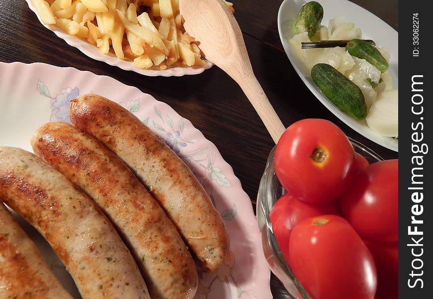 Grilled sausages with marinated tomatoes and cabbage, roast potatoes on wooden table