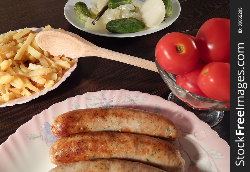 Grilled sausages with marinated tomatoes and cabbage, roast potatoes on wooden table