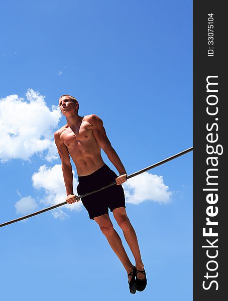 Young strong athlete doing exercise on horizontal bar against blue sky. Young strong athlete doing exercise on horizontal bar against blue sky