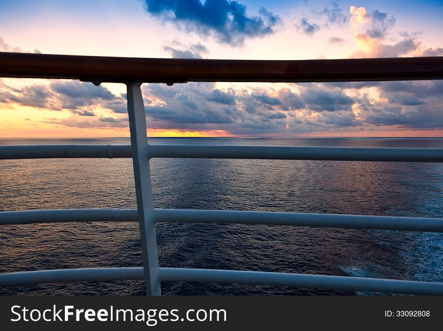 Golden sunset over the Caribbean Sea, through a ship's railing