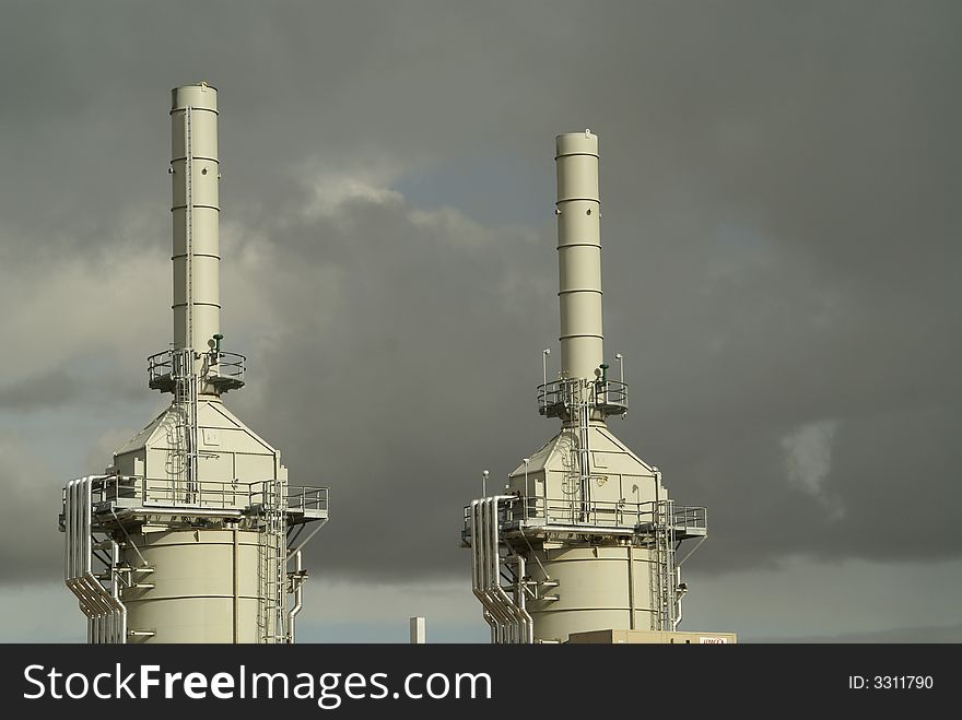 Two towers used in gas processing are highlighted against a dark cloudy sky. Two towers used in gas processing are highlighted against a dark cloudy sky.