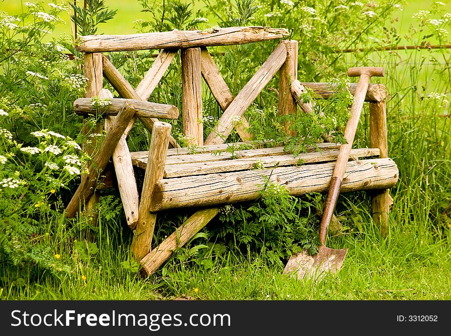 A wooden seat and wooden shovel in a garden setting. A wooden seat and wooden shovel in a garden setting