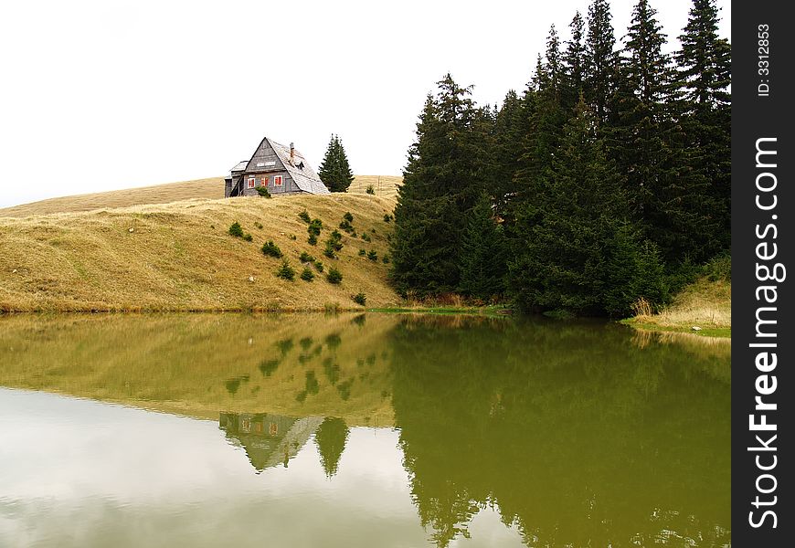 Trees reflecting into the lake water, with hut on the hill. Trees reflecting into the lake water, with hut on the hill