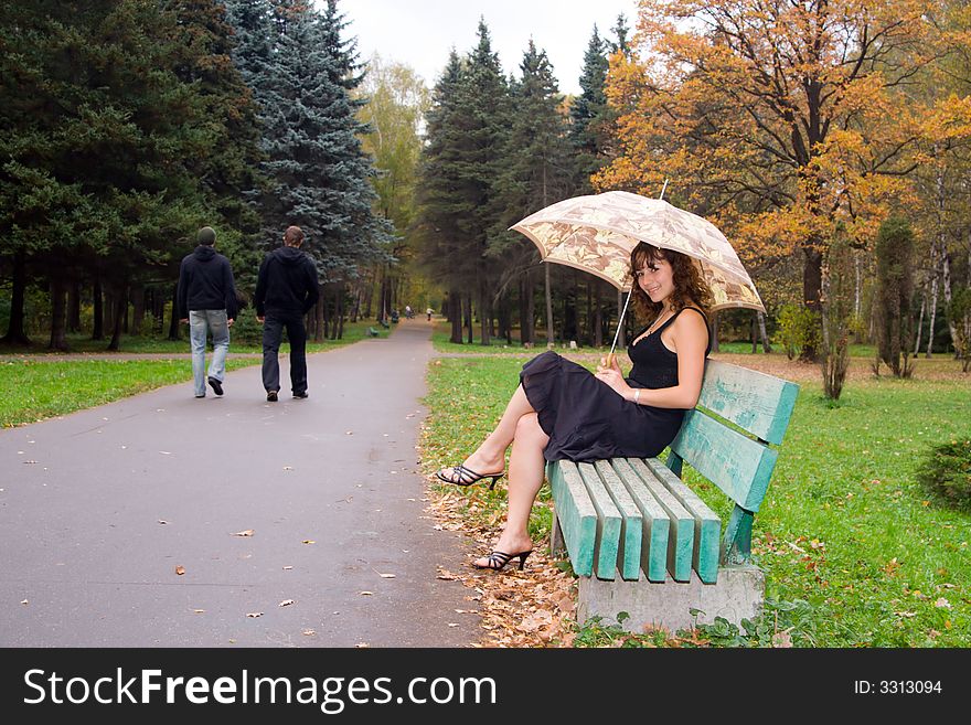 Girl with umbrella sitting on bench at autumn park and smiling.