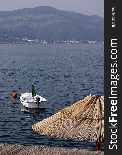 Shot from the terrace of the restaurant at the seaside showing sun umbrella with a boat and sea with mountains at the distance. Shot from the terrace of the restaurant at the seaside showing sun umbrella with a boat and sea with mountains at the distance