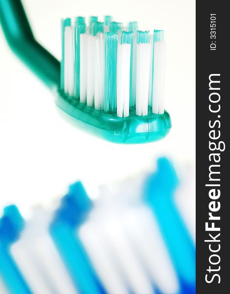 Closeup of two toothbrushes: the first one in focus, the other one out of focus, isolated against white