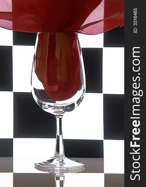 Glass and a red fabric on a checkered black-and-white background. Concept geometry still-life. Glass and a red fabric on a checkered black-and-white background. Concept geometry still-life.